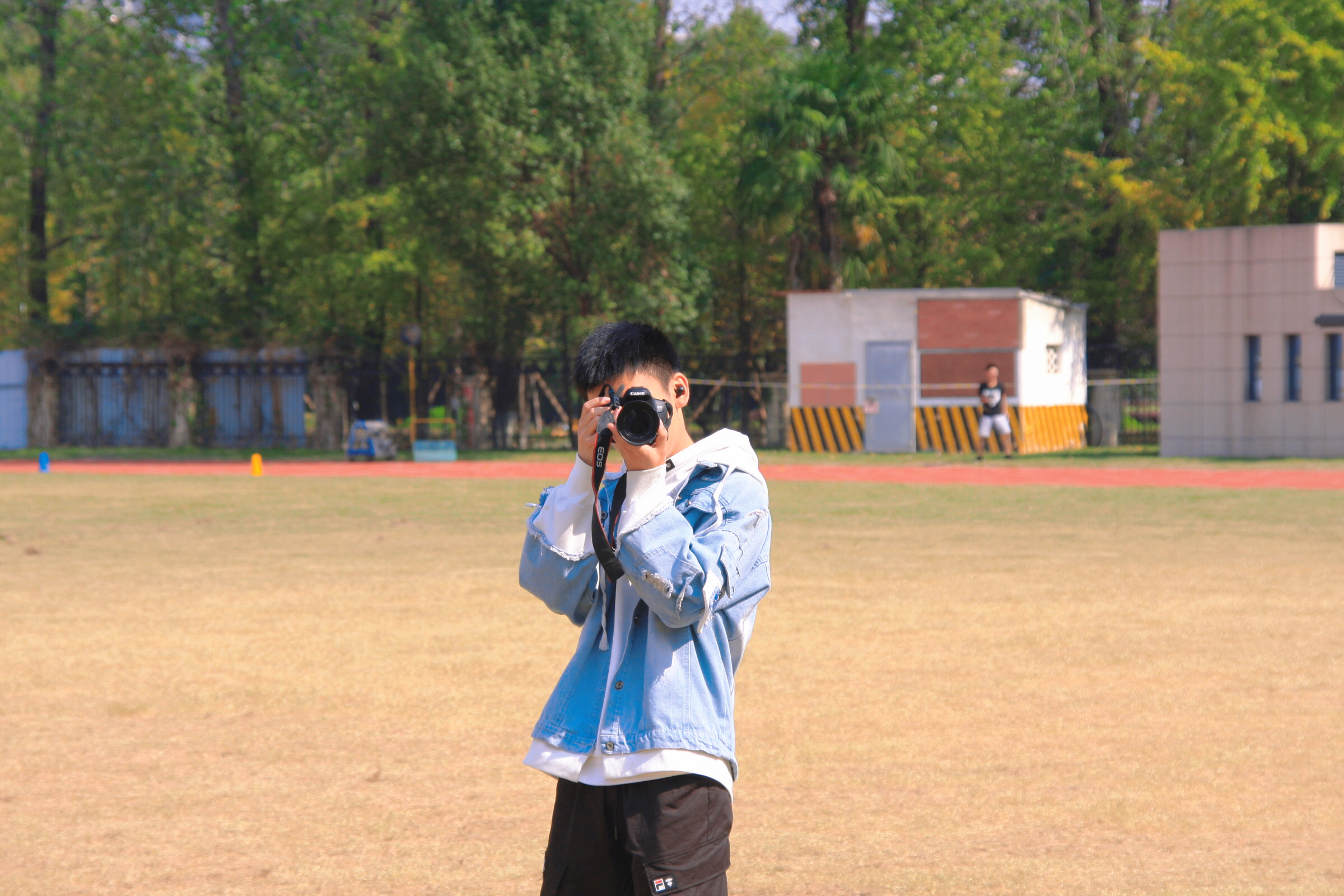 Portrait holding a camera up to the eye on a sunlit school sports field