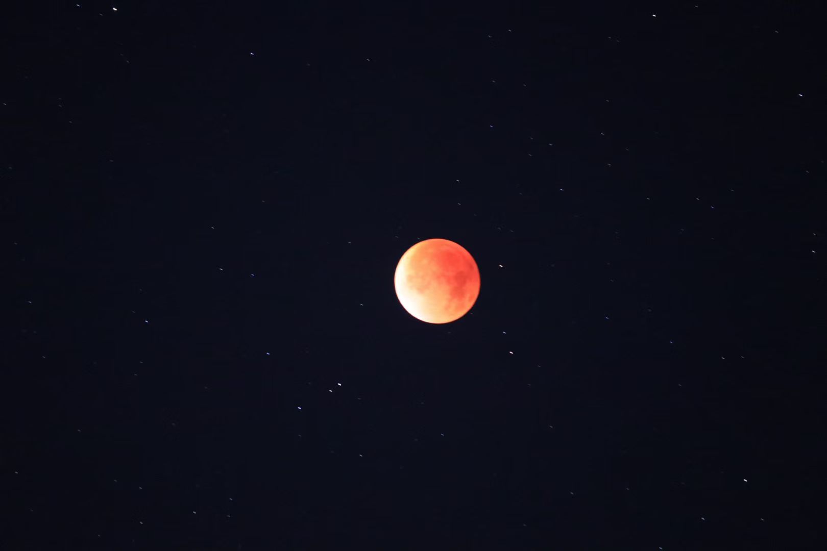 A red-orange blood moon during a total lunar eclipse against a dark starry sky