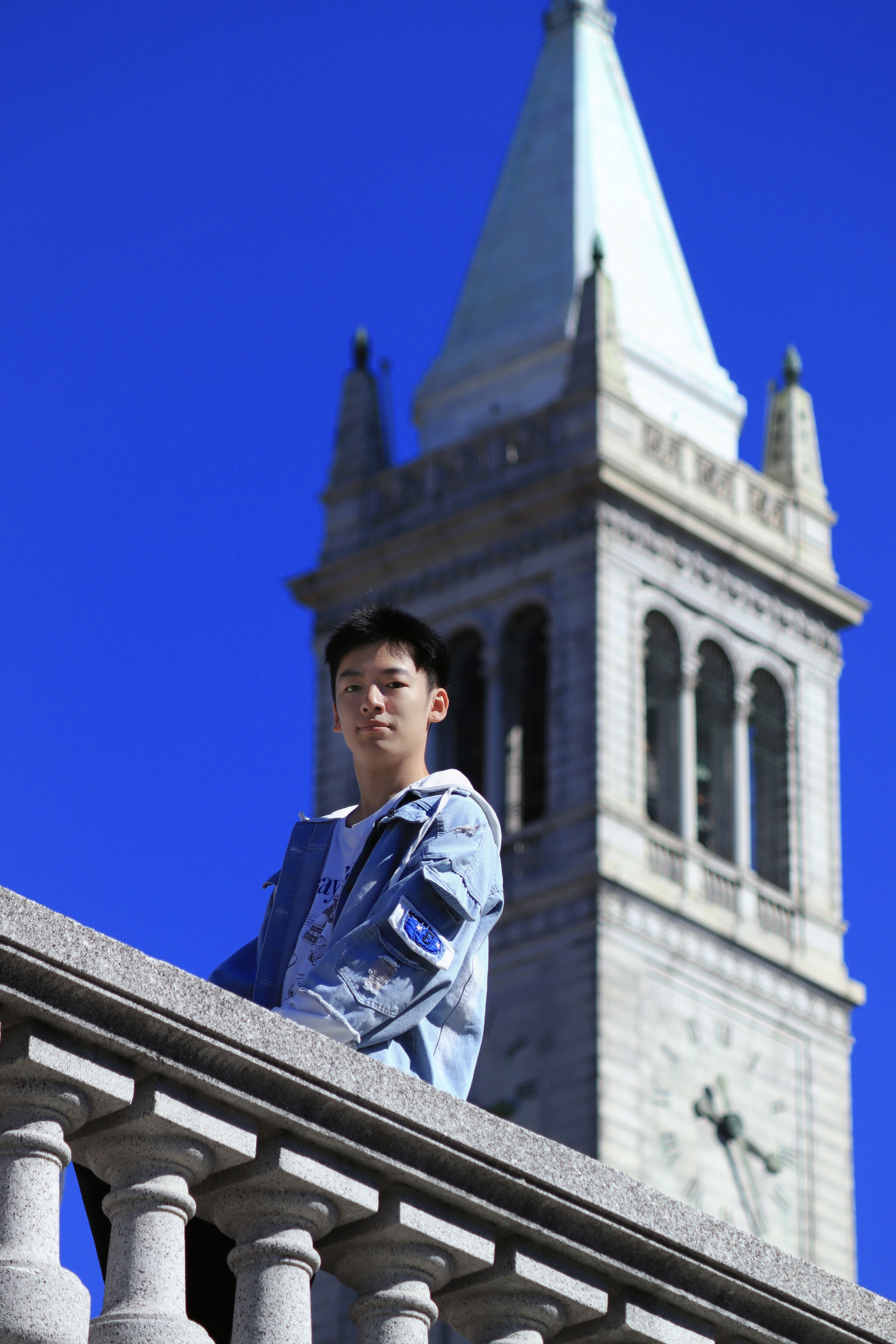 Portrait in a denim jacket on a stone balustrade in front of Sather Tower under a deep blue sky