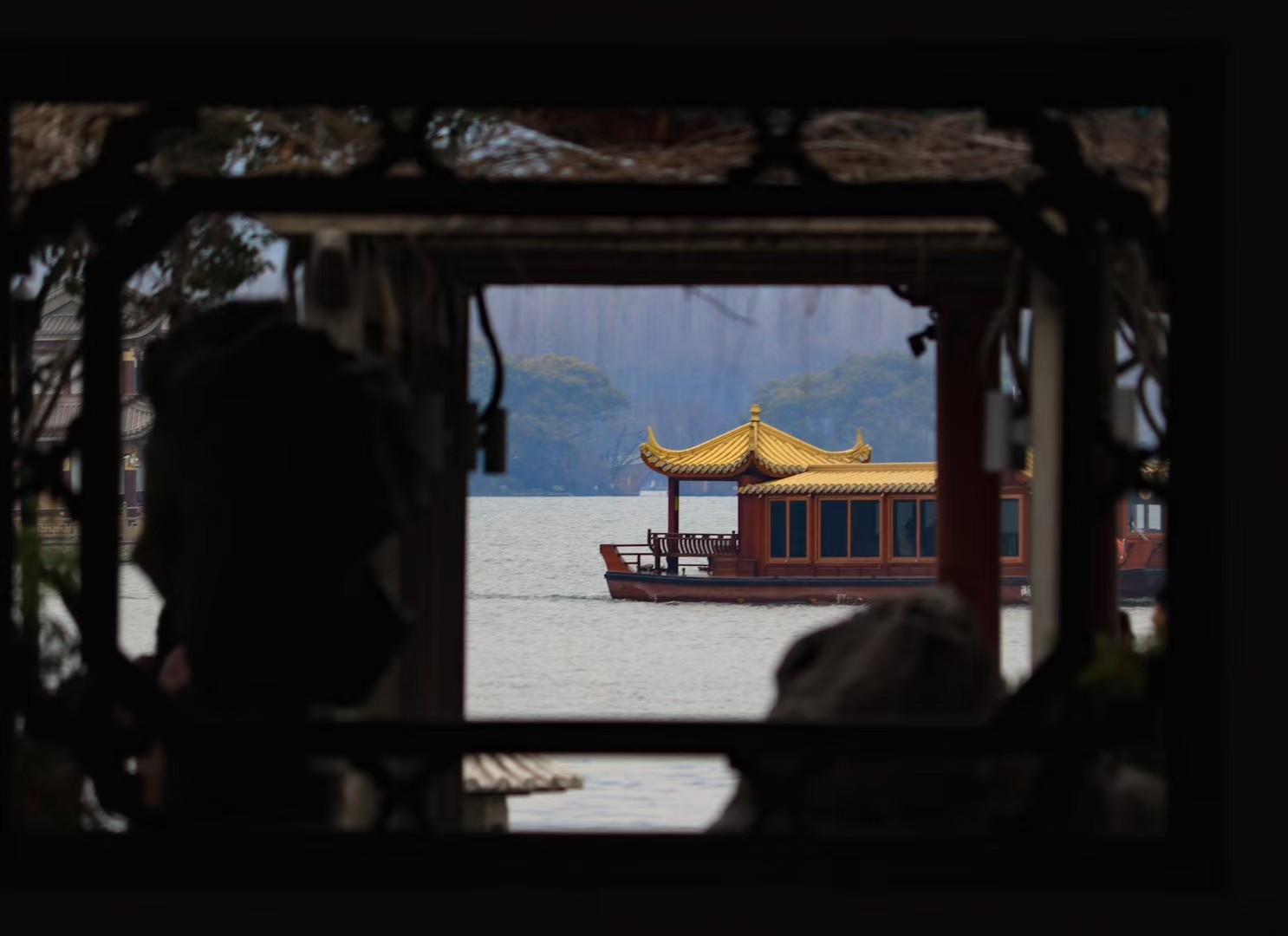 A traditional pleasure boat on West Lake framed by the dark silhouette of a carved pavilion window