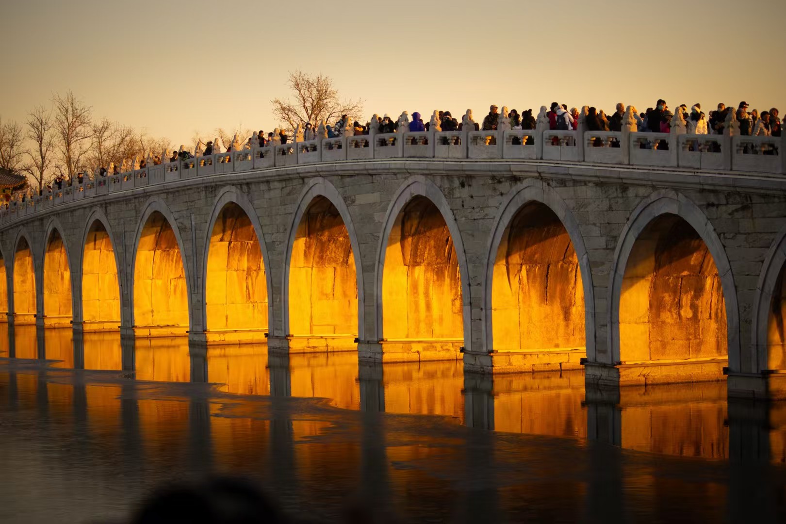 Sunset light glowing golden through the arches of the Seventeen-Arch Bridge, reflected in the icy lake